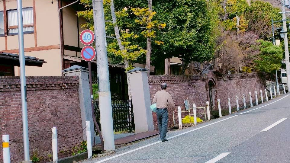 A local walking up a quiet street in Asama Onsen, Matsumoto, carrying a washbasin under one arm